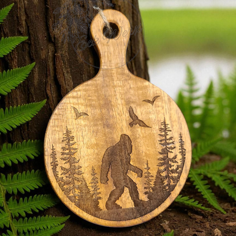 Wooden acacia cutting board with engraved bigfoot design hanging on a tree with nature in the background