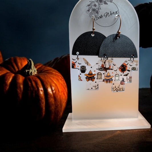 A pair of vintage print Halloween earrings displayed on a stand, featuring designs such as pumpkins, witches, and black cats.